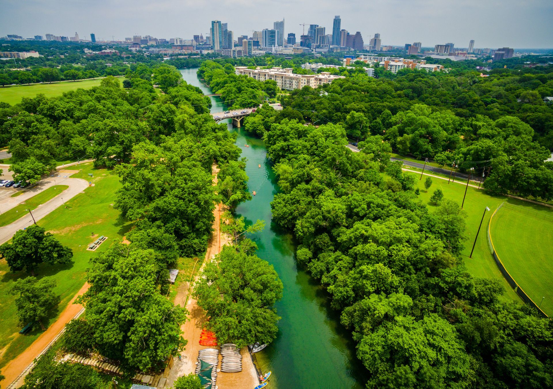 A lush green park with a river running through the center, leading to a distant city skyline under a clear sky.