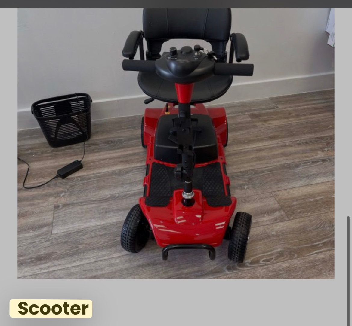 A red, portable mobility scooter with a black seat and a detached basket, parked indoors on a wood-look floor.