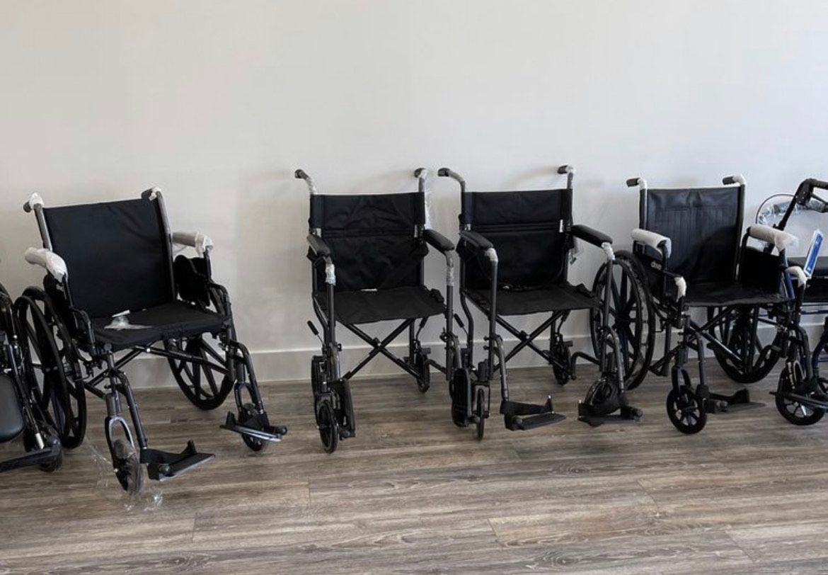 Four black wheelchairs parked in a row against a light-colored wall on a wood-look floor.
