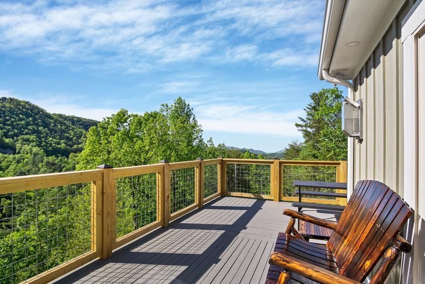 There are two chairs on the deck of a house with a view of the mountains.