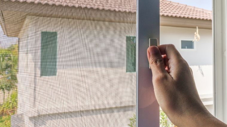 A person is opening a window with a mosquito screen.