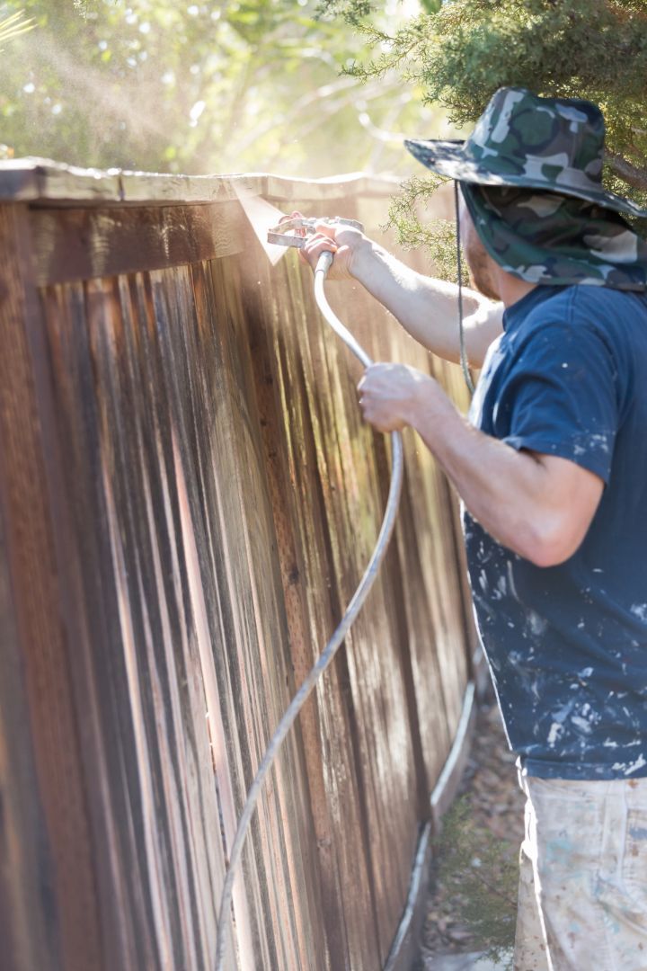 A man is power washing a wooden fence with a hose.