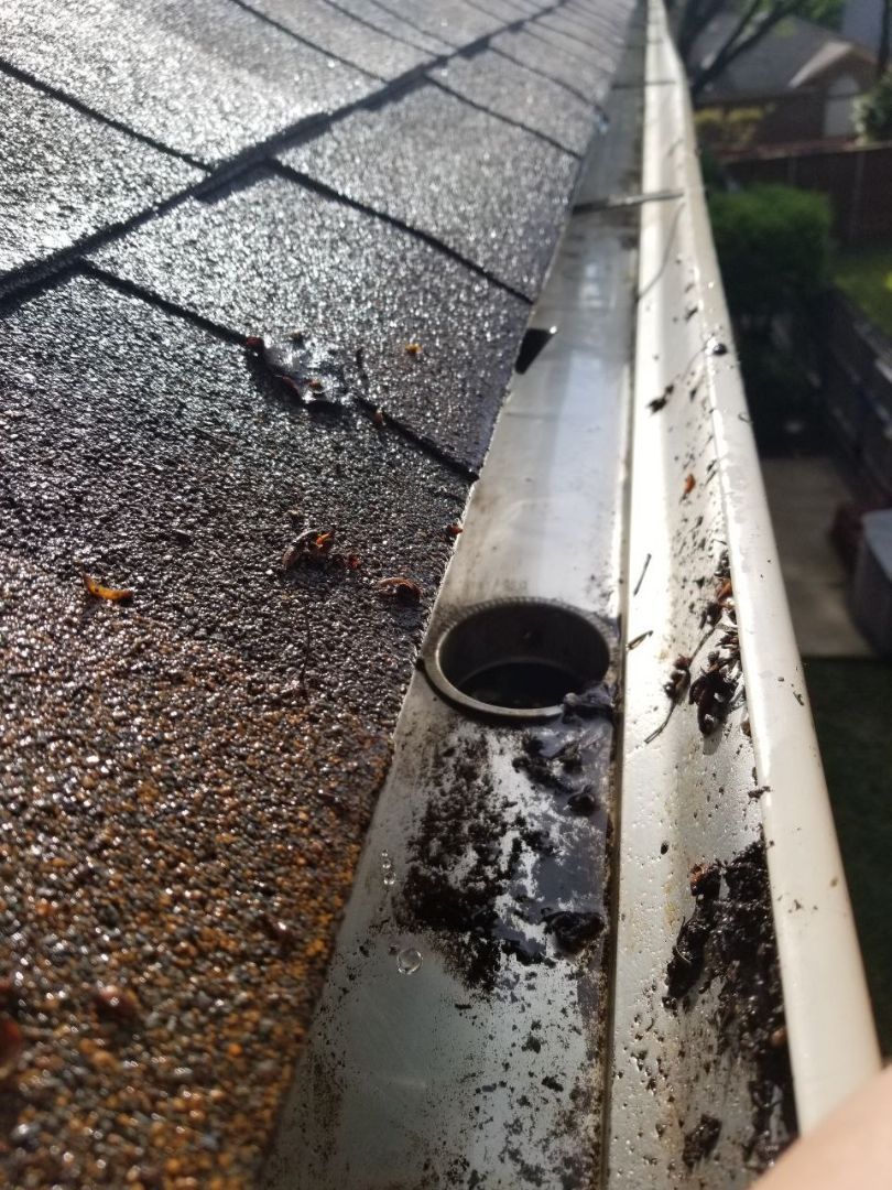 A person is holding a dirty gutter next to a roof.