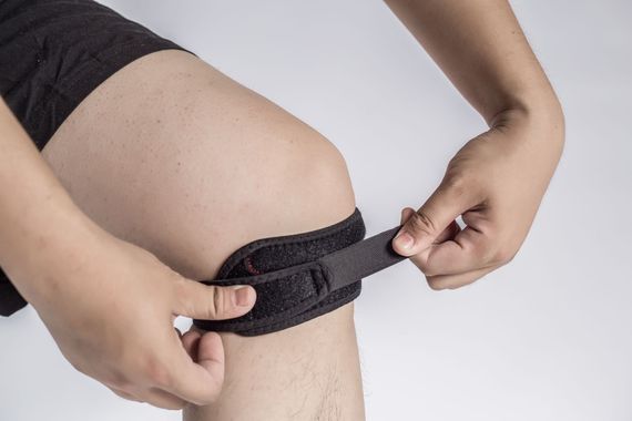 Hands fastening a black knee brace on a leg with visible skin irritation