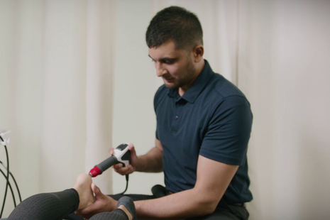 Therapist using a handheld massage tool on a patient’s foot in a clinic setting