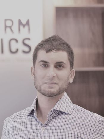 Portrait of a man in a checkered shirt standing indoors beside shelves and a wall sign