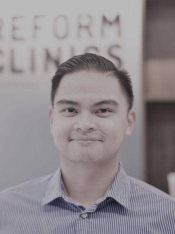 Portrait of a smiling man in a striped shirt standing in front of a blurred office sign