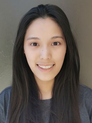 Smiling person with long dark hair against a plain gray background
