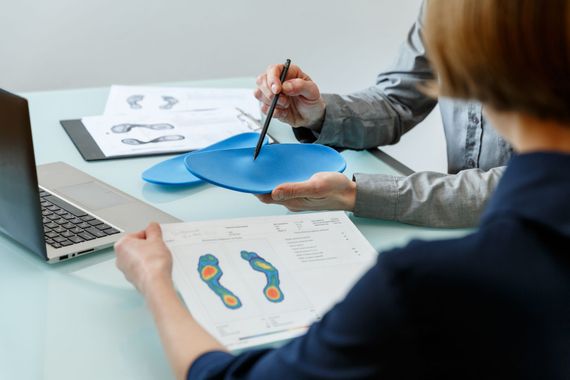 Two people reviewing foot pressure maps and a blue orthotic model at a desk with a laptop