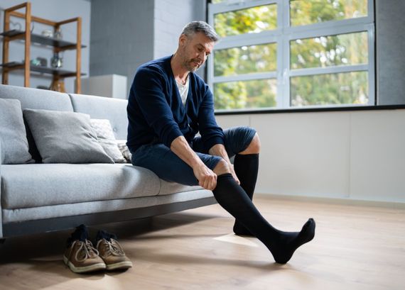 Man sitting on a sofa putting on a black sock in a bright living room