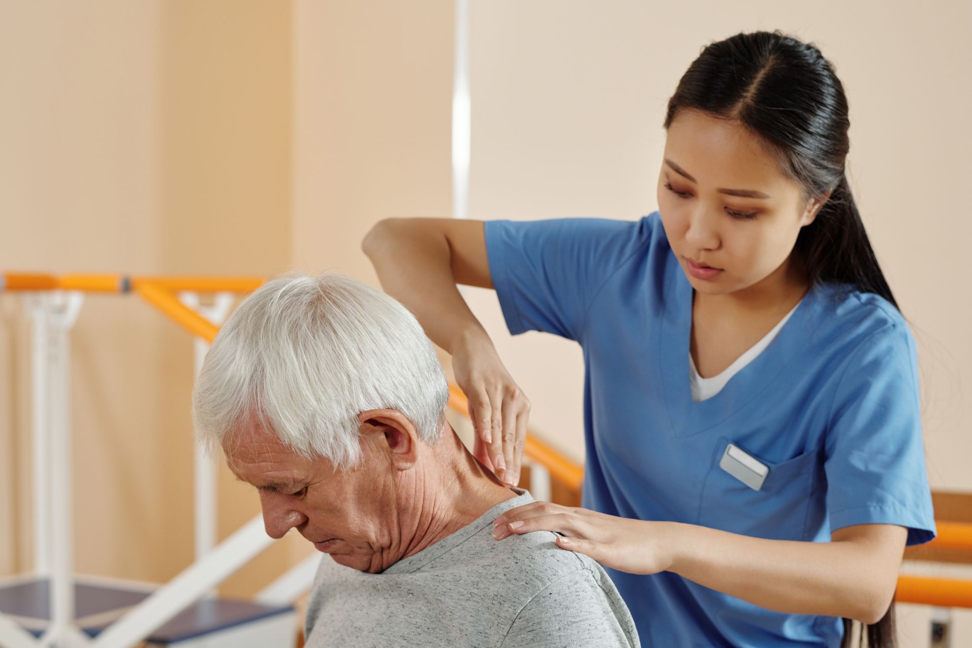 Caregiver in blue shirt massages an older person's shoulders in a bright room