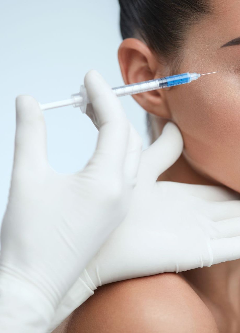 Person receiving an injection near the eye. Medical professional in gloves holds a syringe.