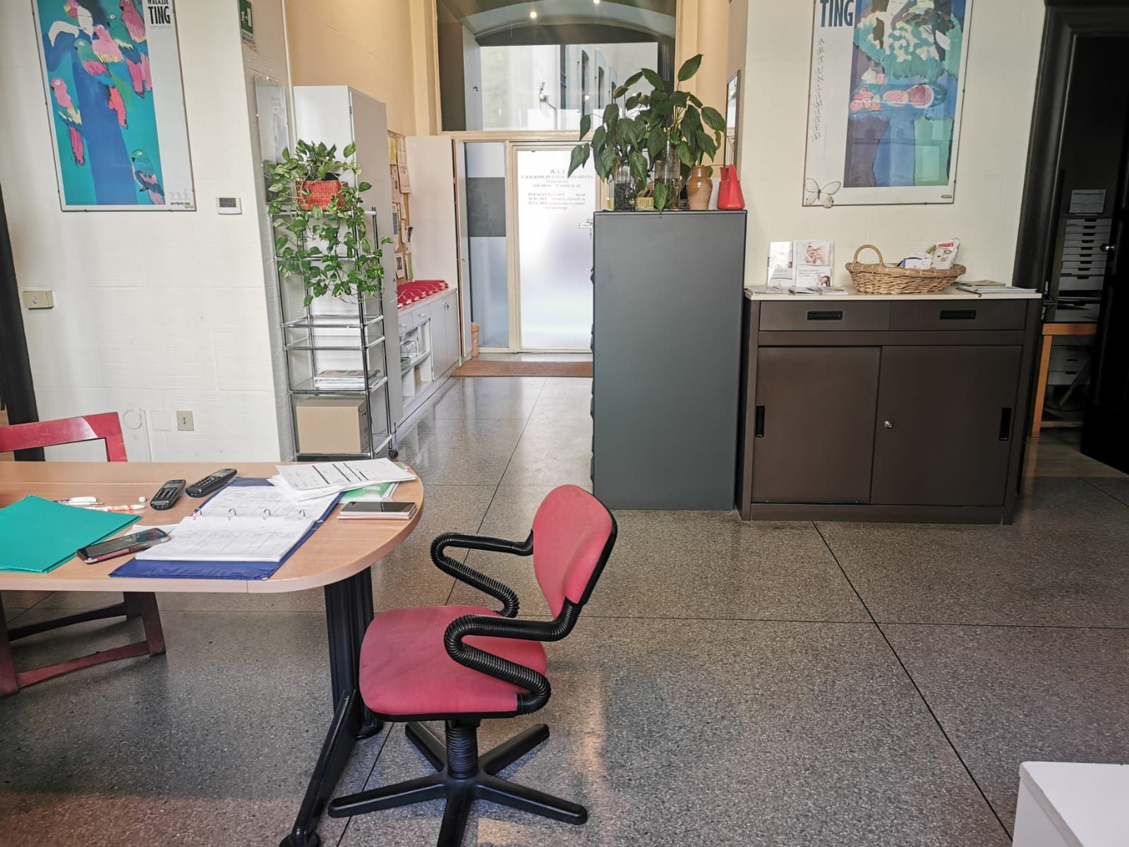 Interno di un ufficio con scrivania, sedia, armadietti e ingresso.