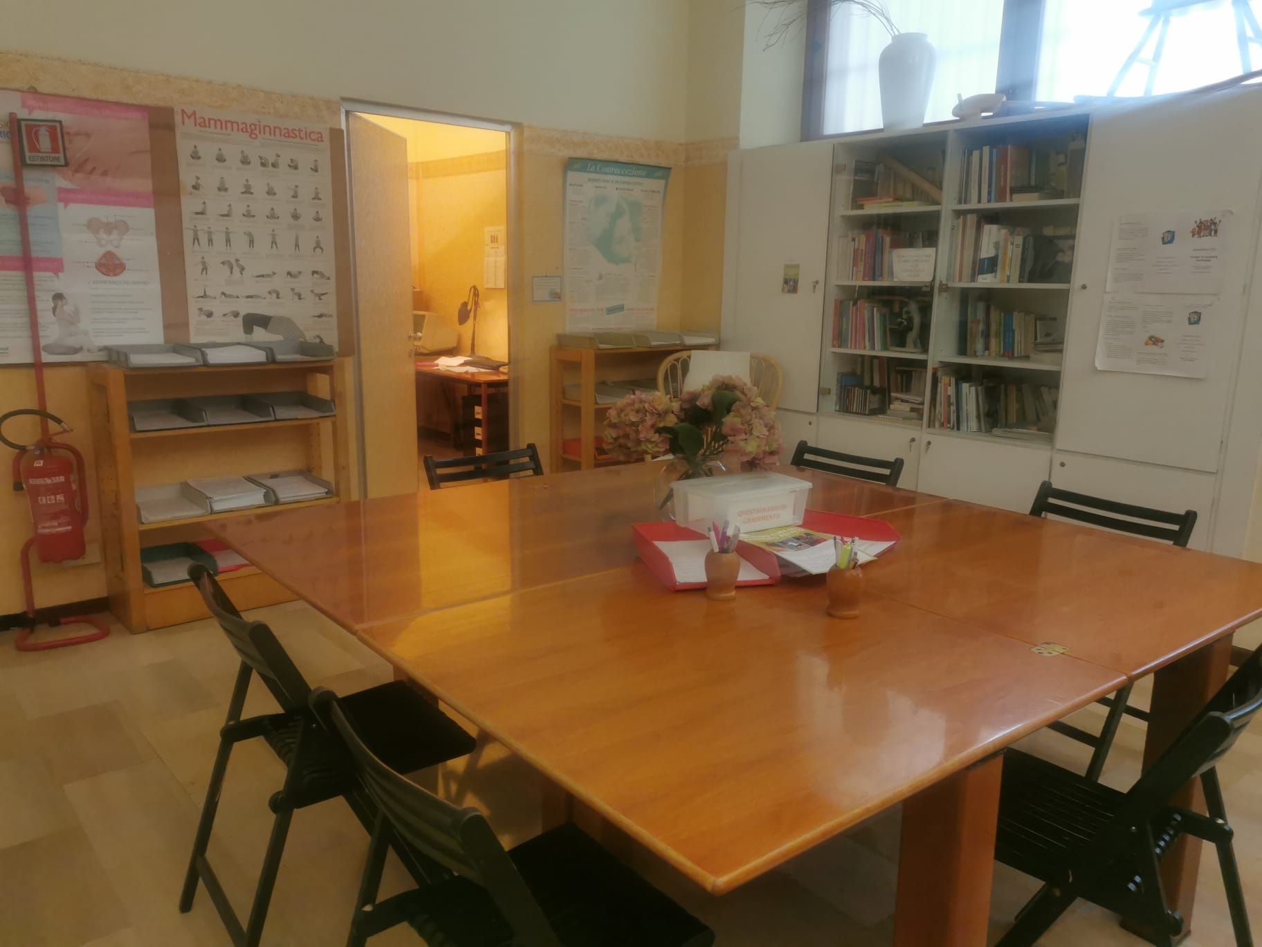 Una stanza con un grande tavolo di legno, sedie, una libreria e una porta che conduce a un'altra stanza.