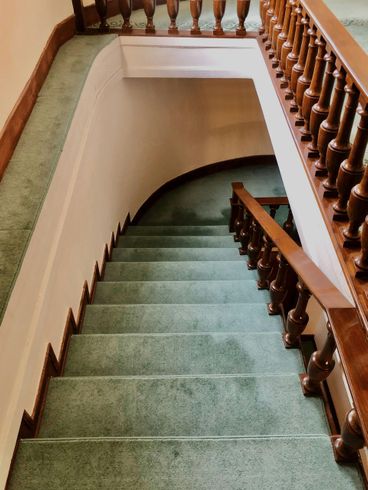 Staircase with green carpet, wooden handrails, and a curved landing.