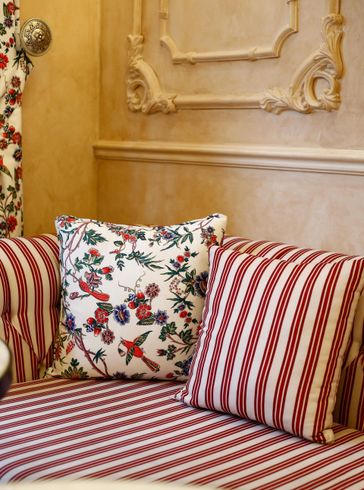 Couch with red and white striped fabric and floral and striped pillows, against a tan wall.