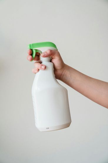 Hand holding white spray bottle with green trigger.