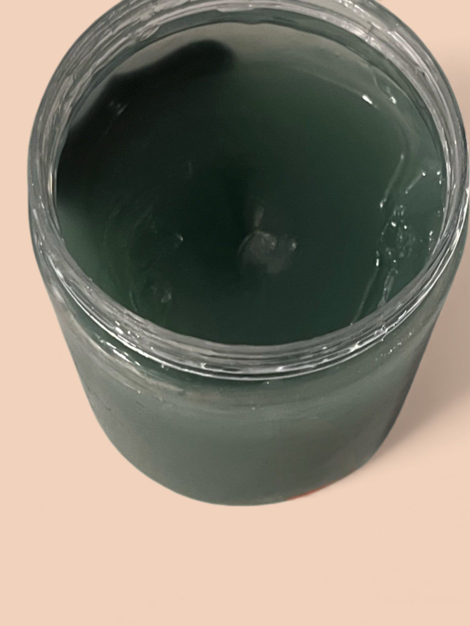 Open jar filled with dark green paint or gel on a light surface