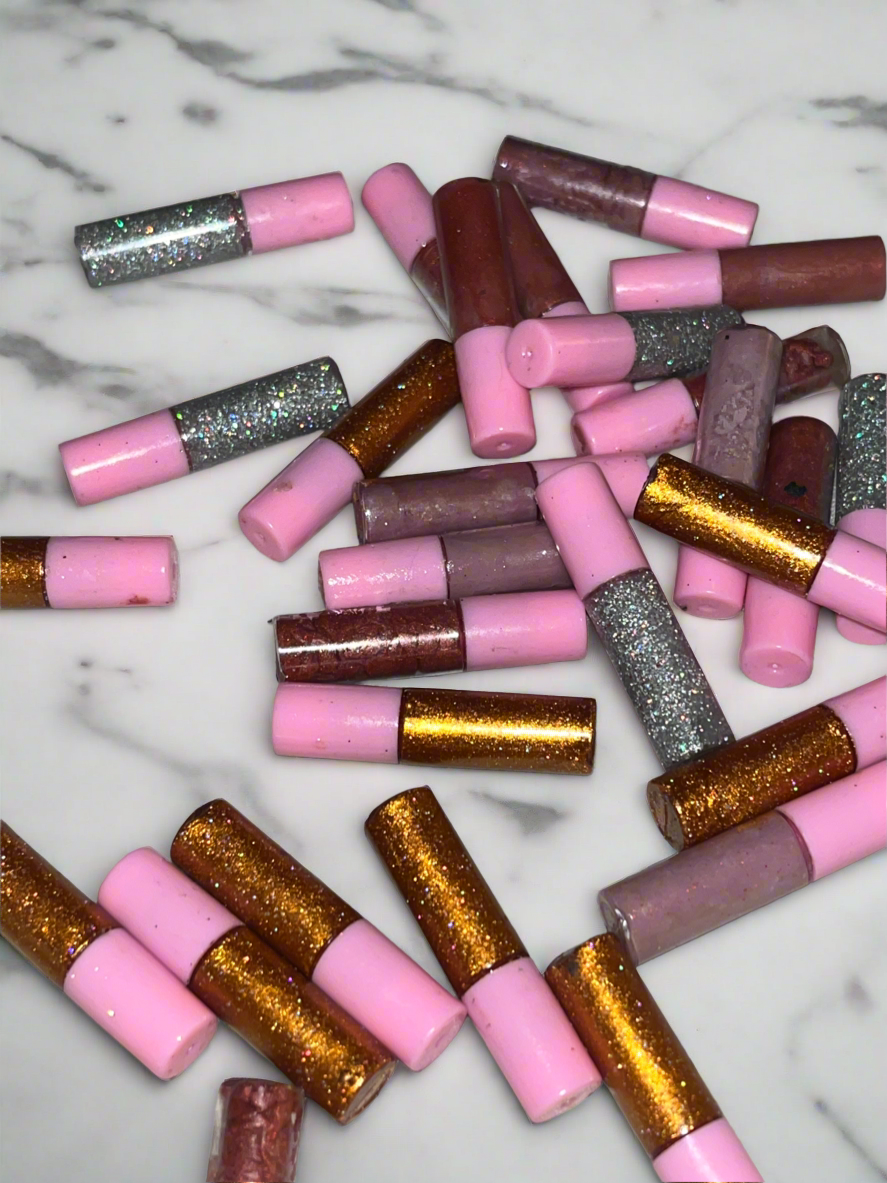 Scattered pink, silver, and gold glittery cylindrical pieces on a white surface