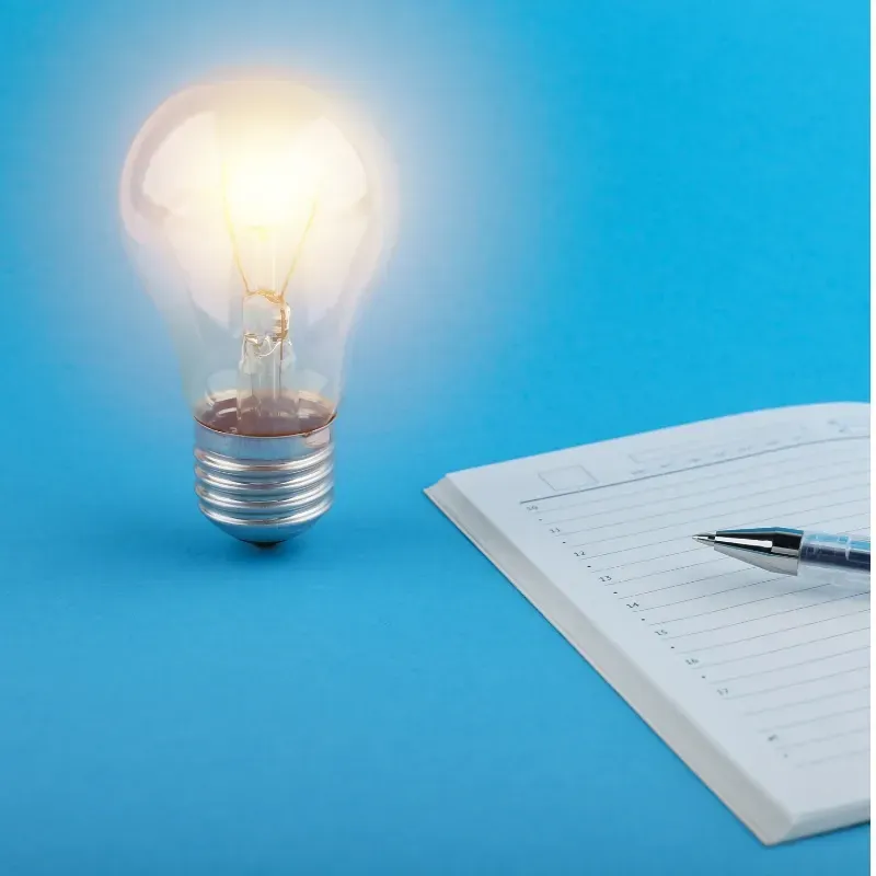 A light bulb is sitting on top of a notebook next to a pen.