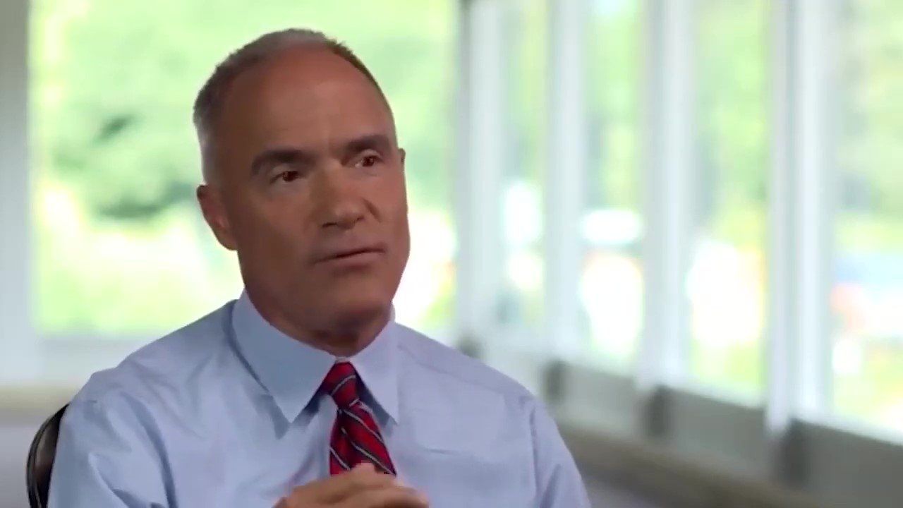 A man in a blue shirt and red tie is sitting in front of a window.