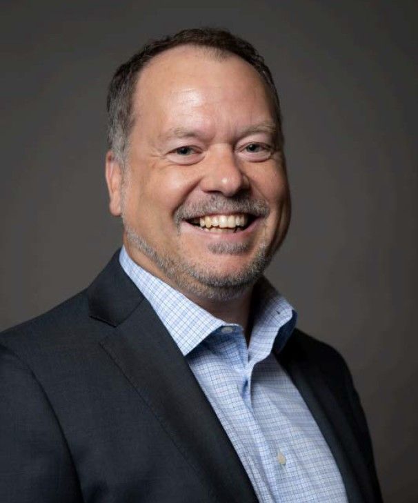 A man in a suit and blue shirt is smiling for the camera.