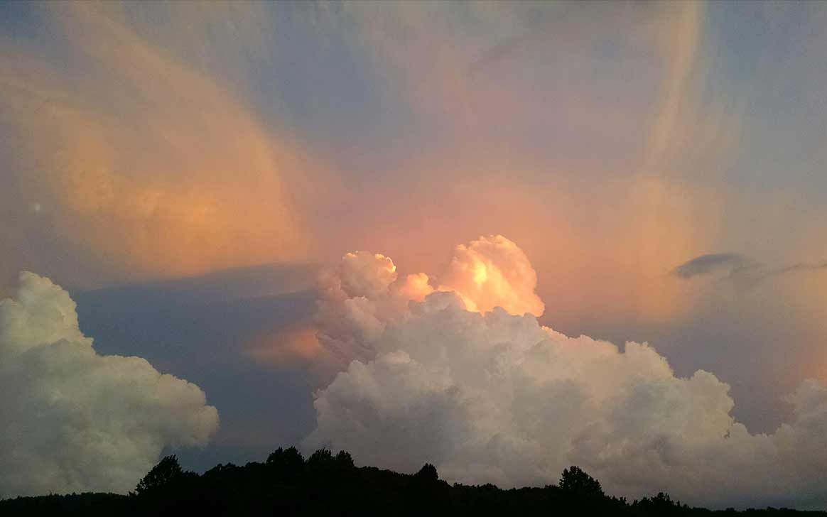 A sunset sky with a lot of clouds and trees in the foreground.