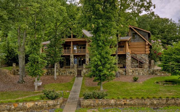 A large log cabin is surrounded by trees and grass