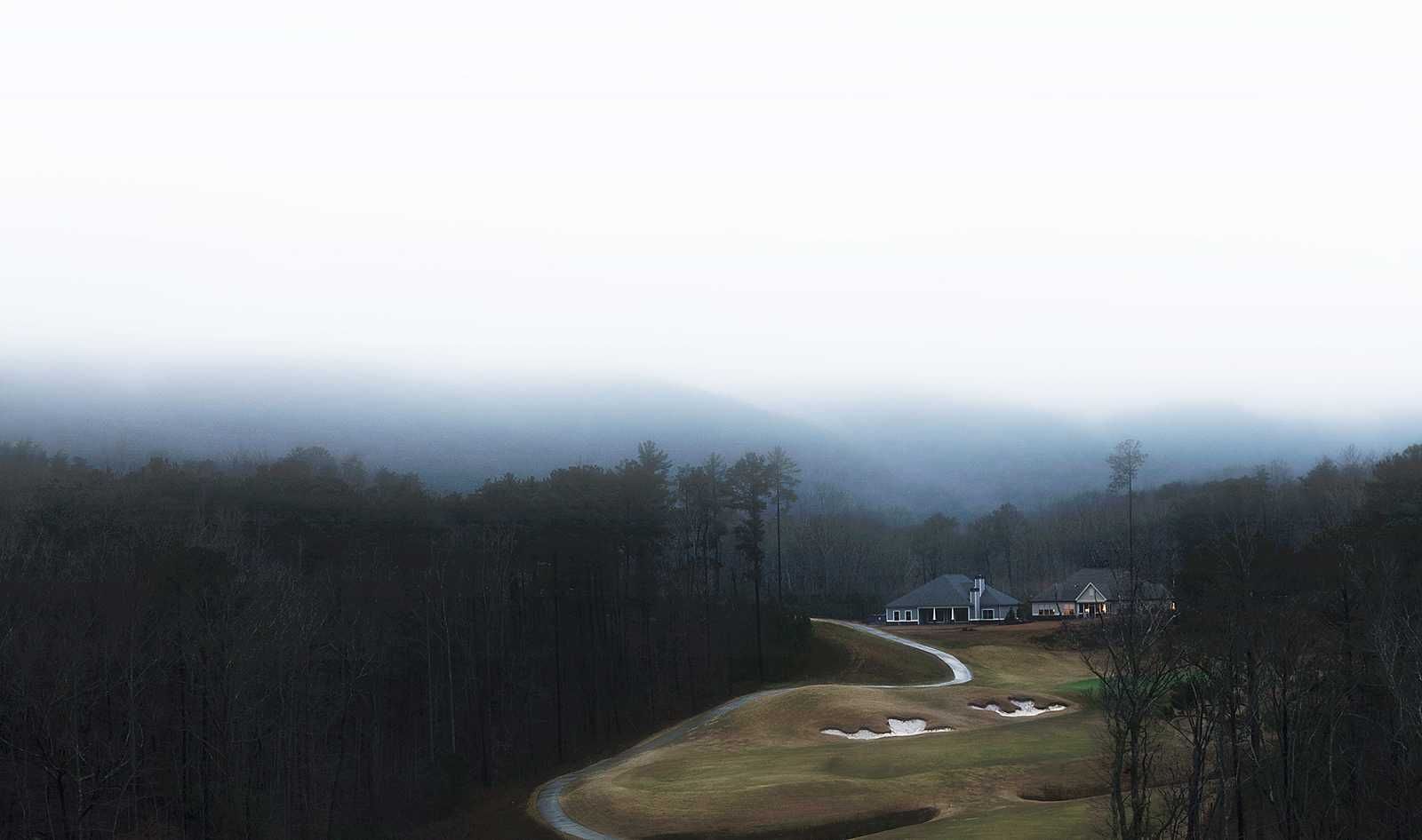 A house is sitting on top of a hill in the middle of a foggy forest.