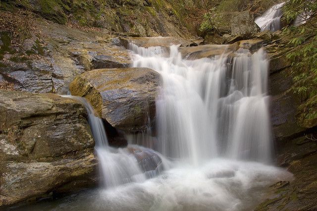 A waterfall is surrounded by rocks and trees in the woods.