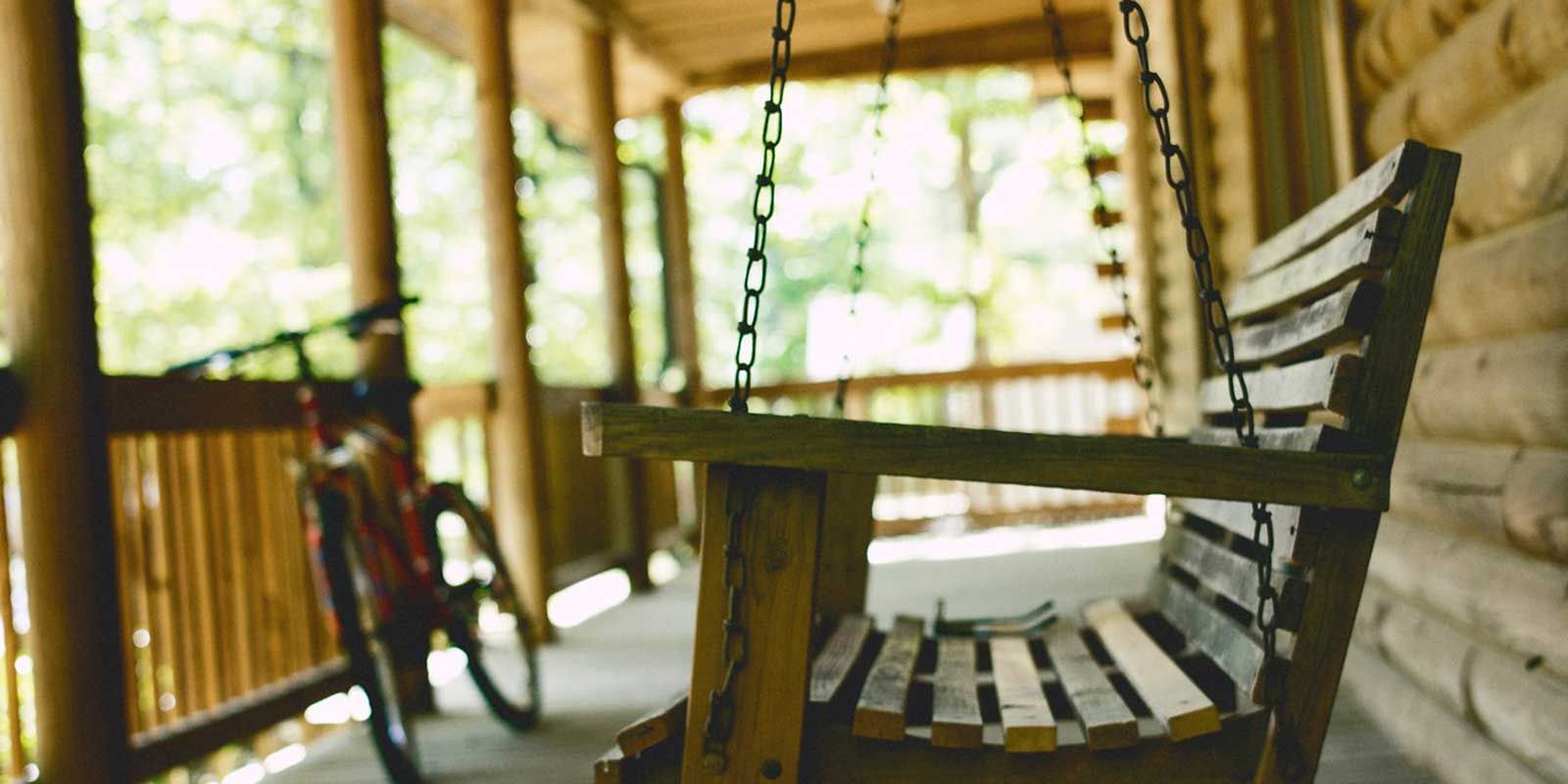 A wooden porch swing with a bicycle in the background.