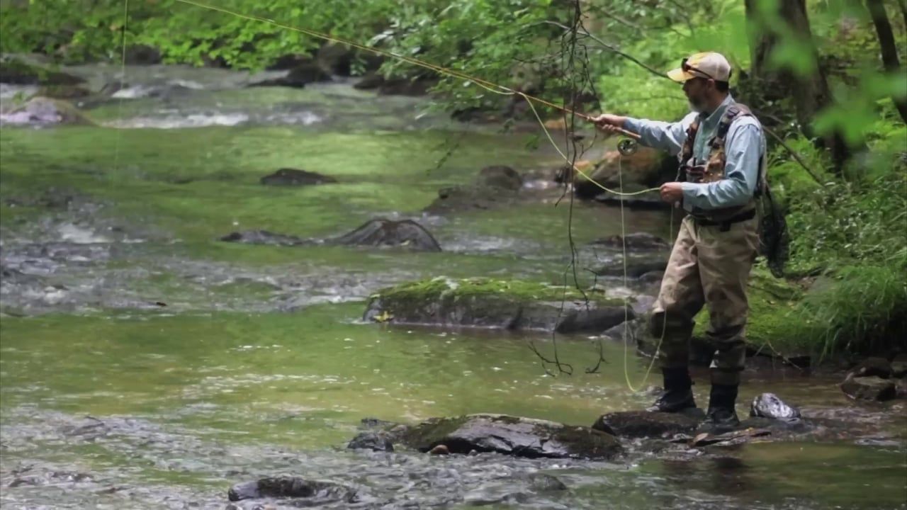 A man is fishing in a river while standing on a rock.