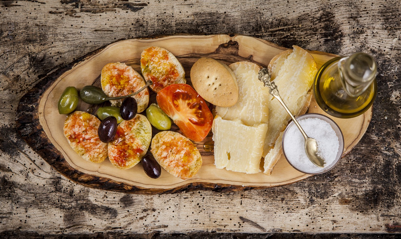 Una taula de tallar de fusta coberta amb pa , olives , tomàquets , formatge i sal.