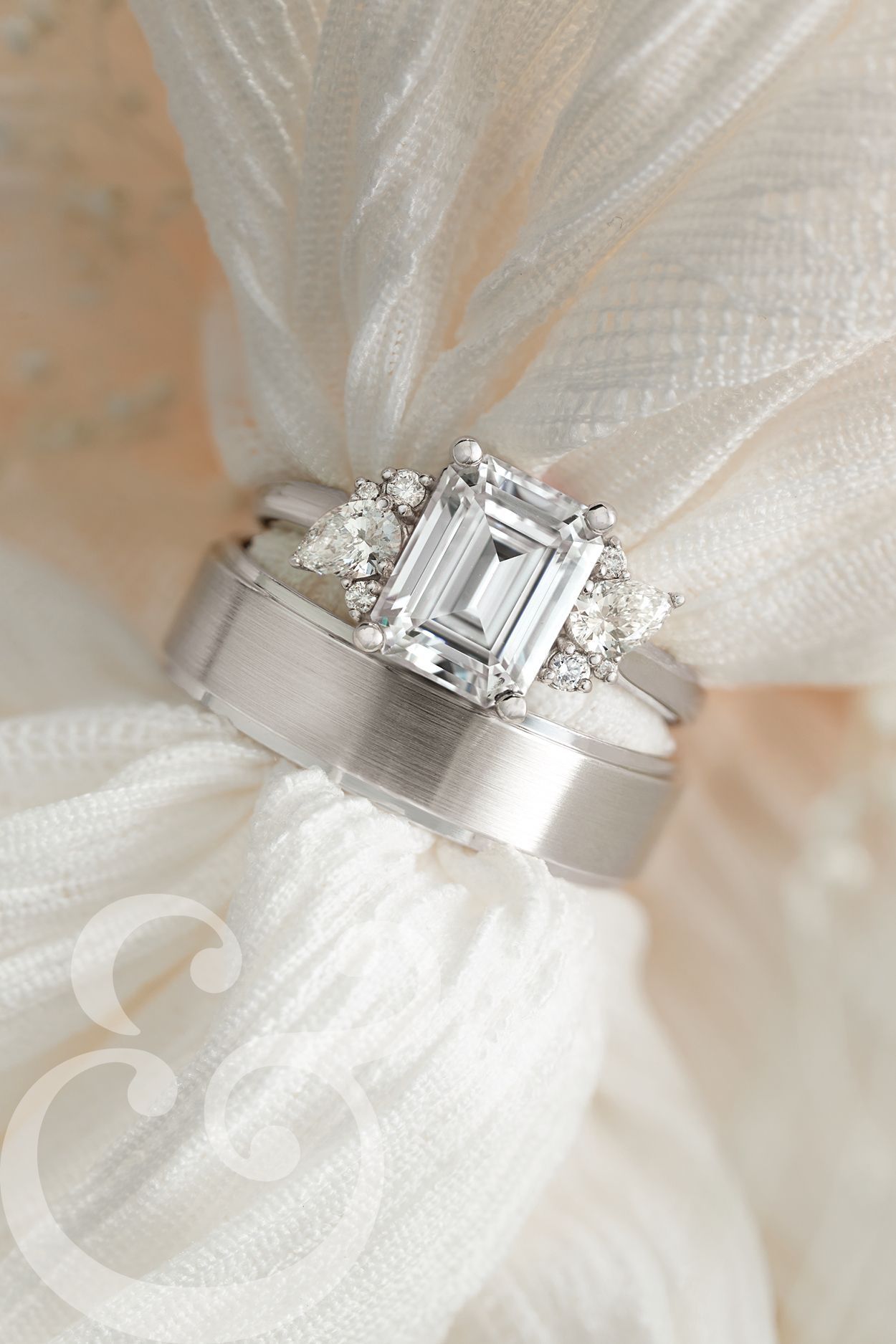 A close up of a wedding ring and engagement ring on a white cloth.