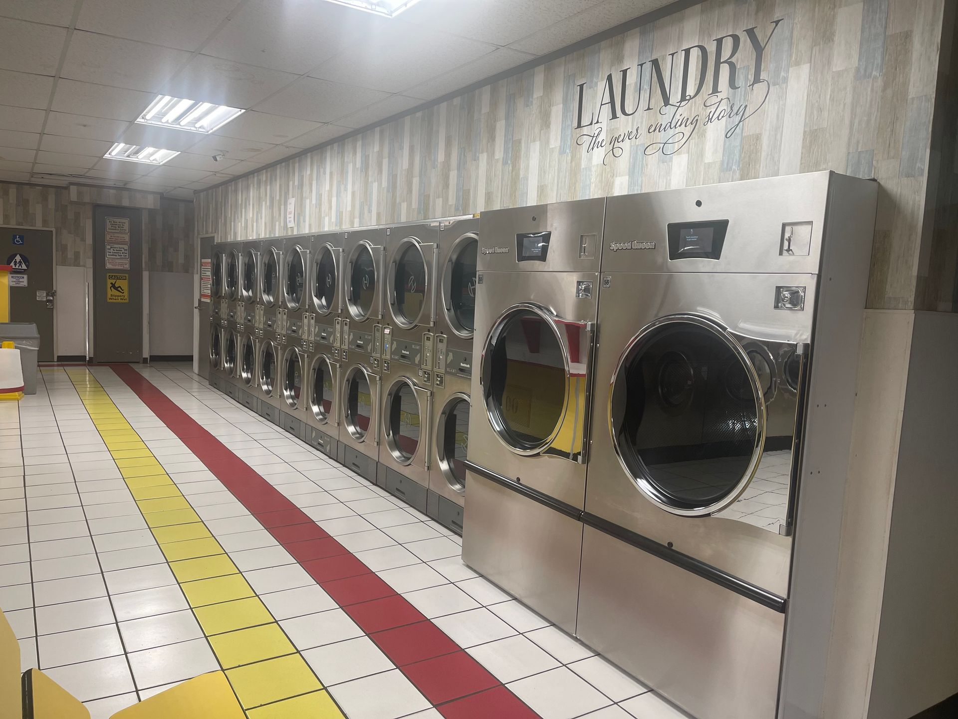 A laundromat with rows of washing machines, a red and yellow tiled floor, and the word