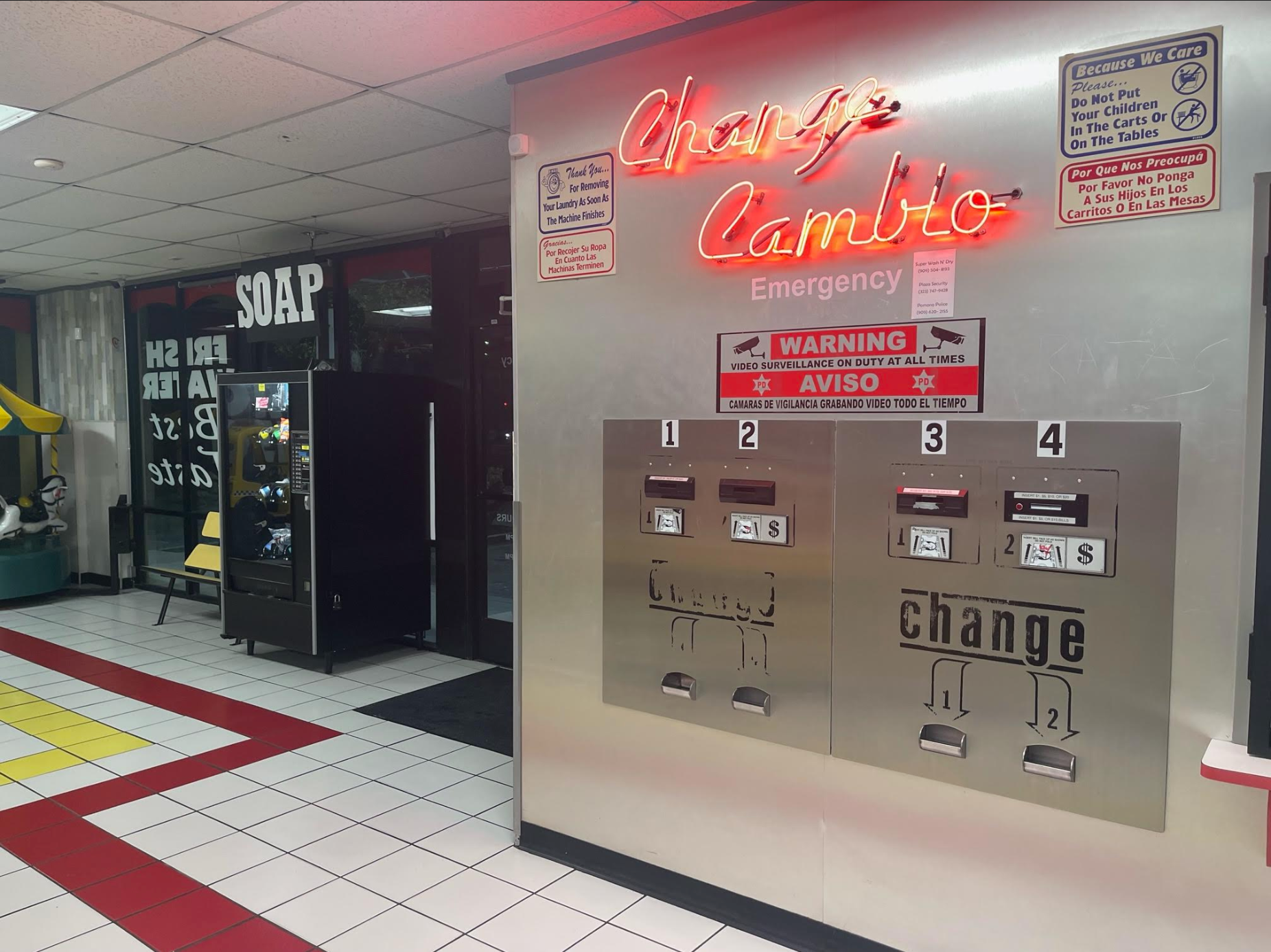 Change machine in a laundromat; red neon sign, metallic panels, vending machine, and tile flooring.
