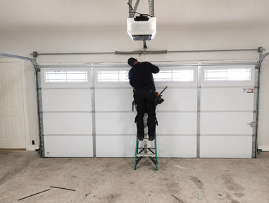 Person standing on a ladder installing a garage door opener in a garage