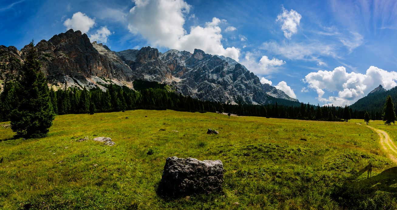 Sunny green meadow with rocky mountains and blue sky with clouds in the background