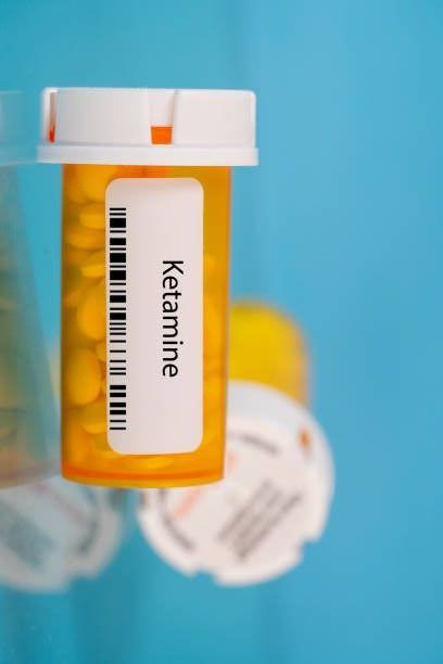 Amber prescription bottle labeled “Ketamine” on a blue background.
