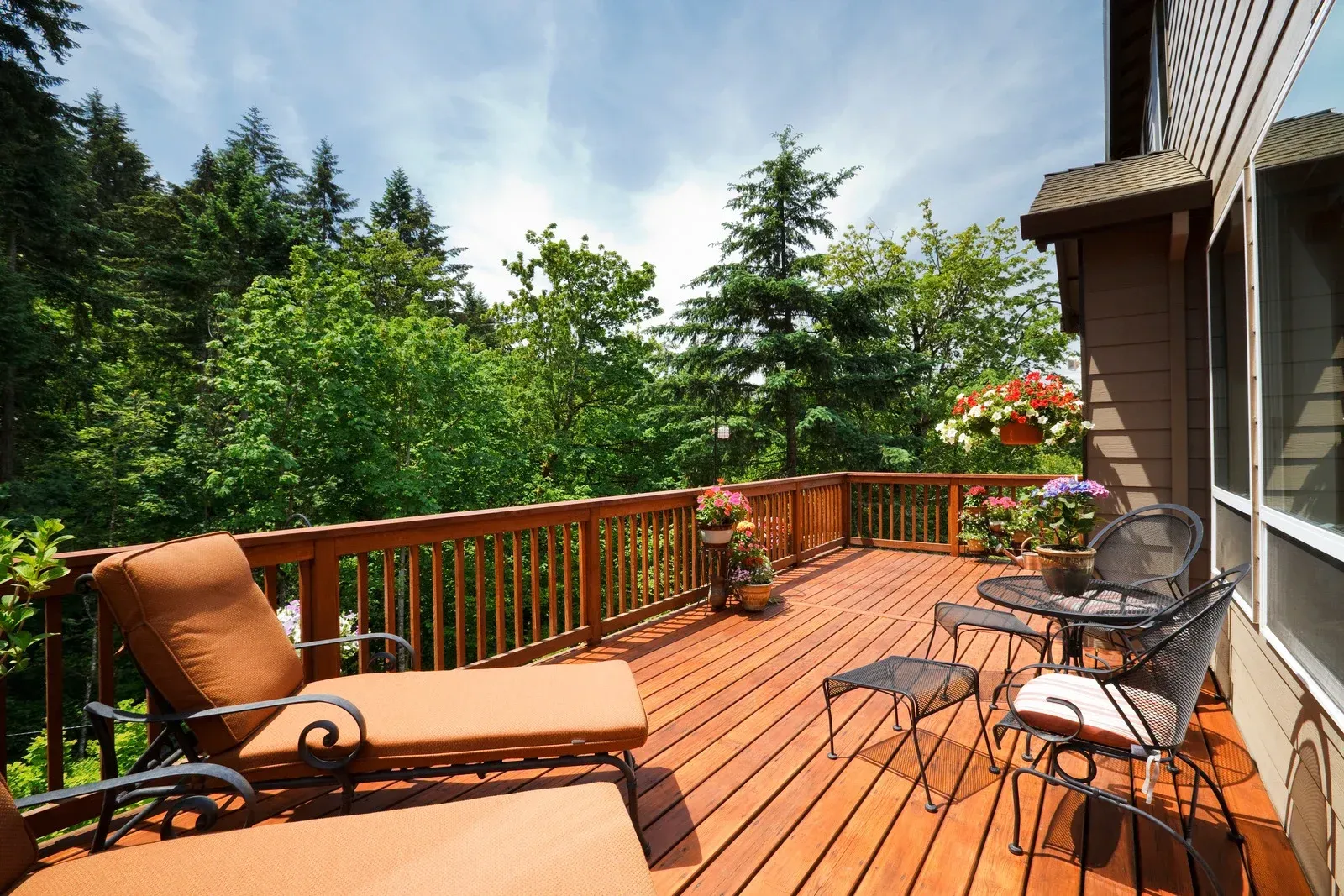 Wooden deck with lounge chairs and a small table overlooking lush green trees under a sunny sky