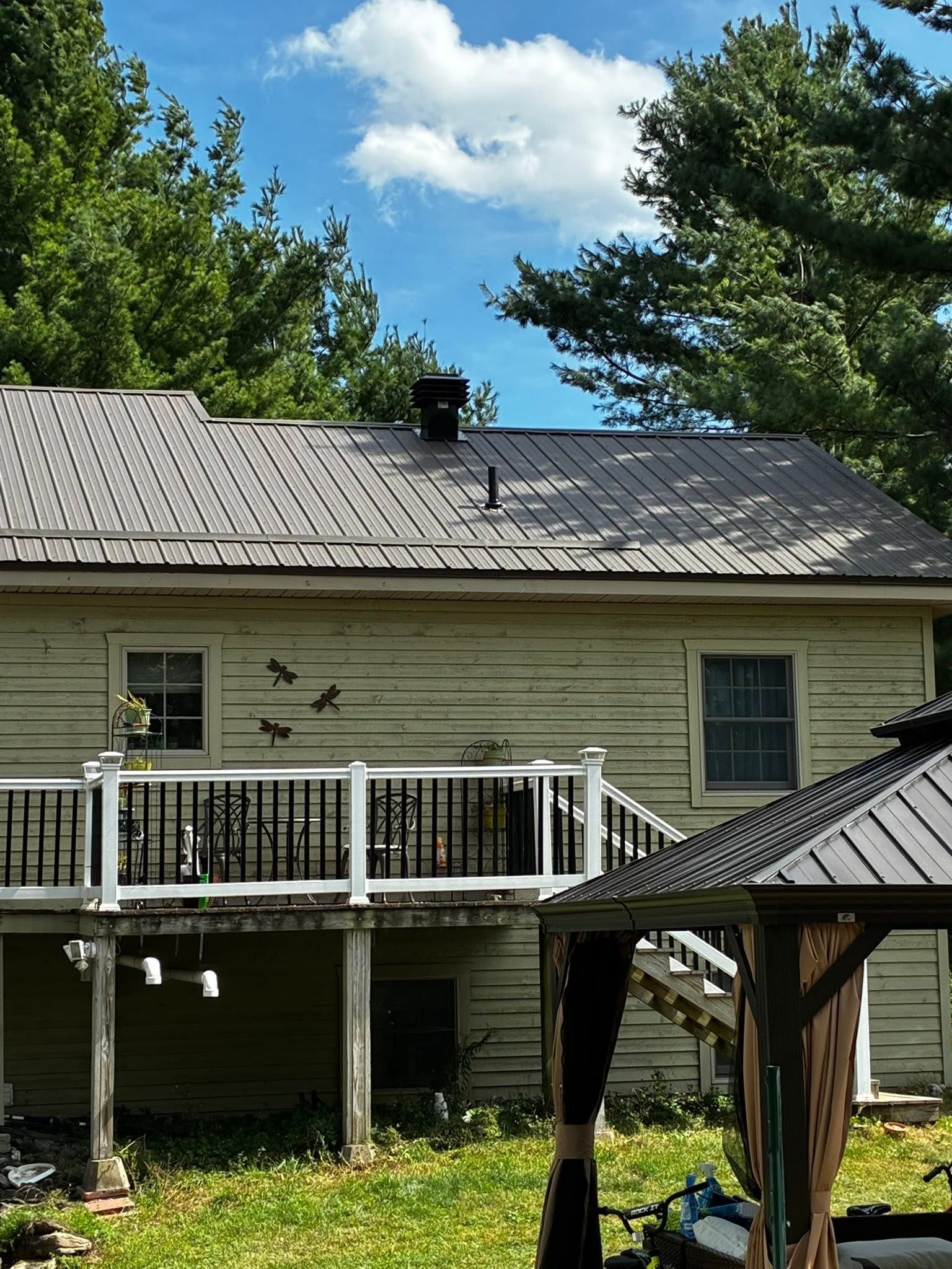 Back of a house with a white deck, gray roof, and backyard trees under a blue sky