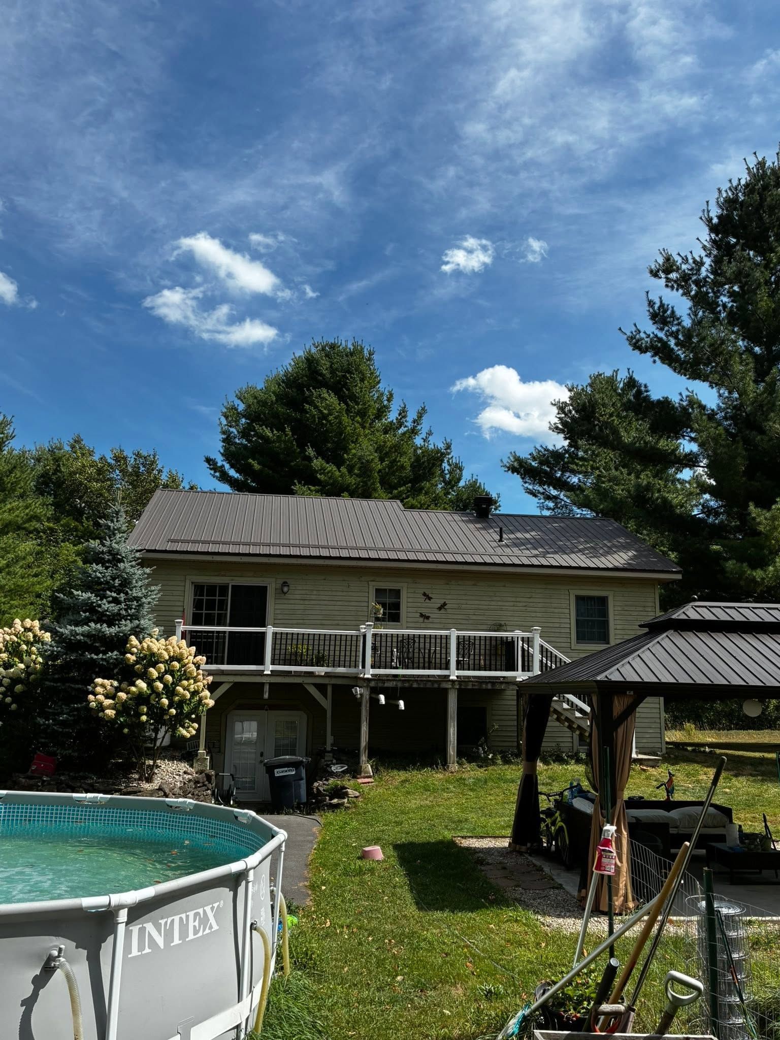 Backyard with above-ground pool and raised deck beside a house under a blue sky