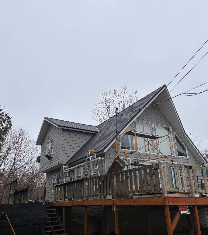 Gray house under construction with scaffolding and a wooden deck on a cloudy day