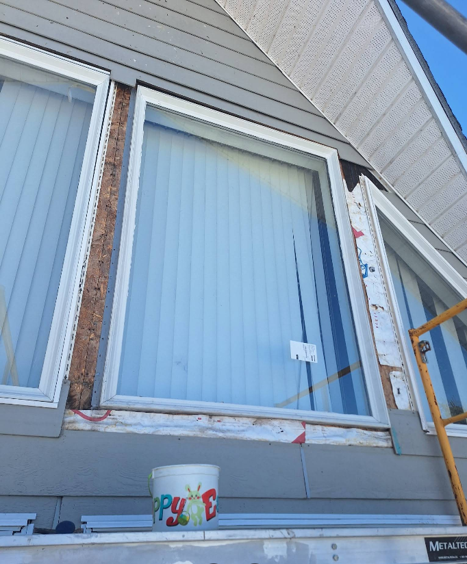 House exterior with a large window taped off for renovation and a paint bucket below