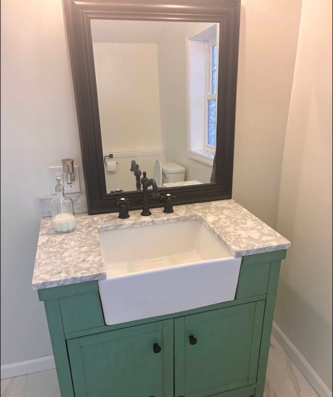 White sink vanity with marble top, dark mirror, and teal cabinet in a bathroom corner