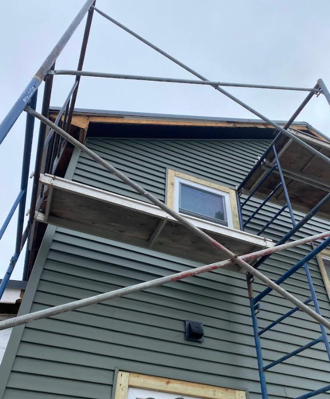 Scaffolding around a gray house exterior with a small window under the roofline
