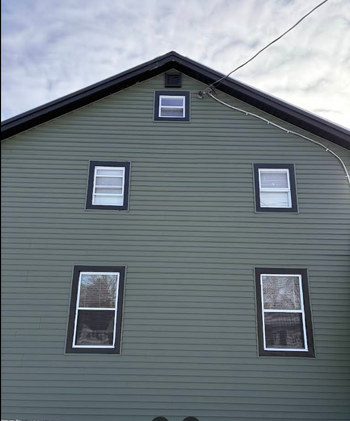 Gray house exterior with green siding and five windows under a steep gabled roof.