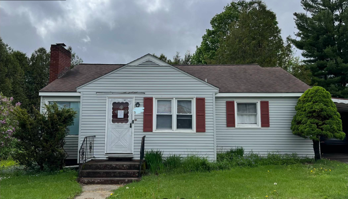 Small white single-story house with red shutters and a front porch under cloudy skies
