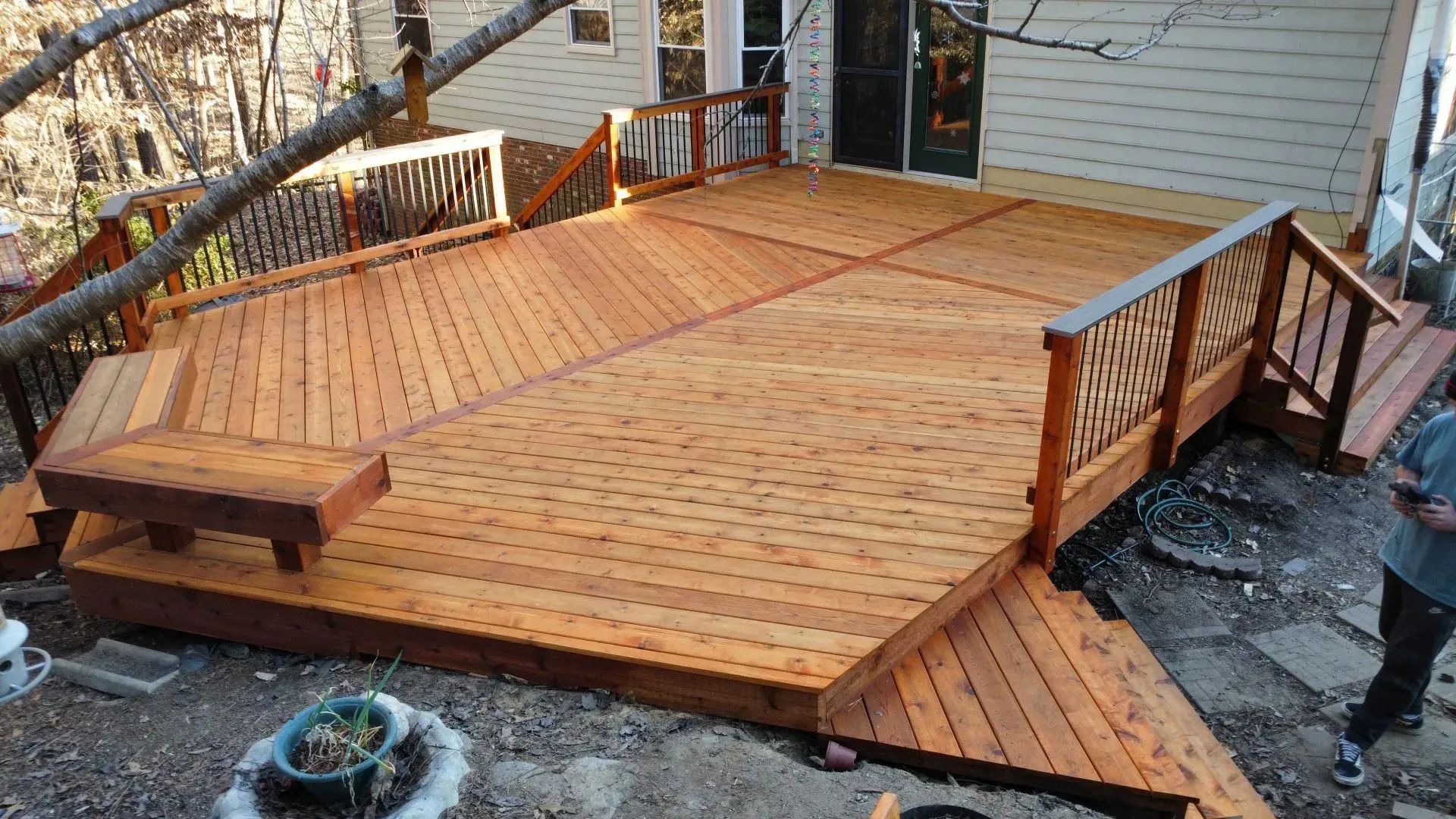 Wooden backyard deck under construction beside a house, with railing sections and steps.