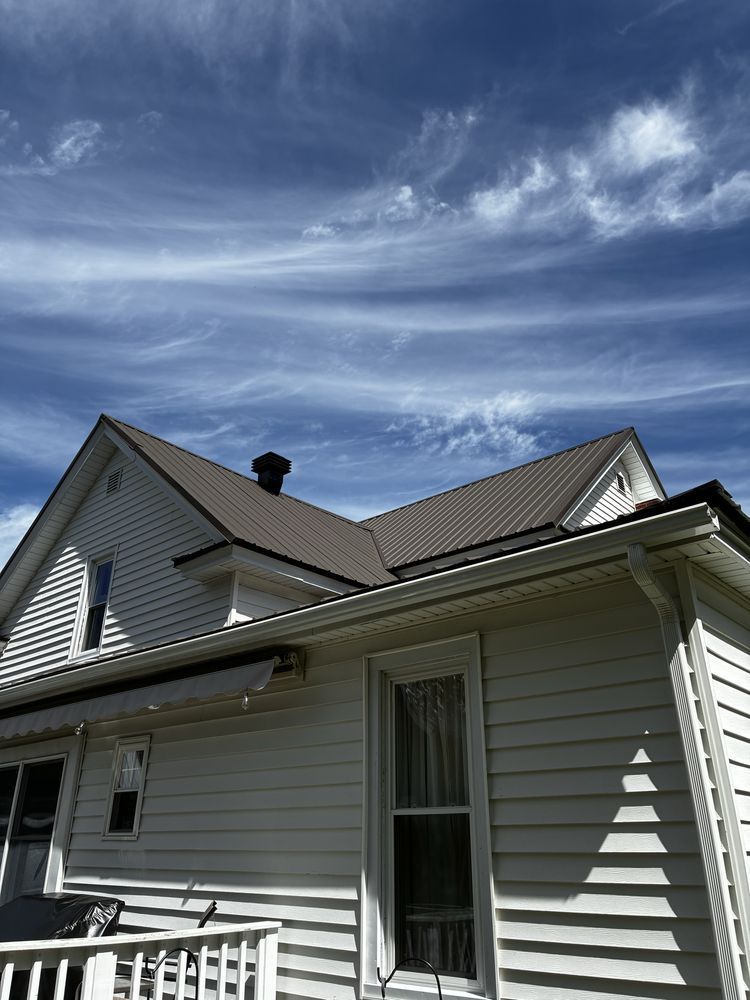 House with light siding and metal roof under a blue, cloud-streaked sky